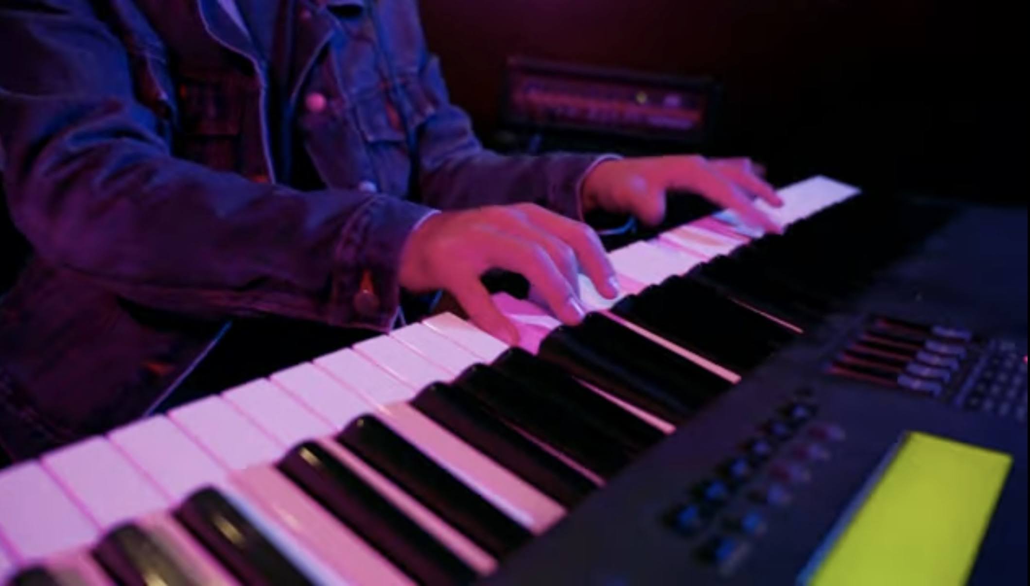 Chad Tamayo playing keys in a dark, neon-lit studio